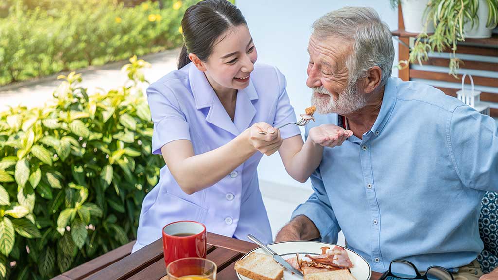 A caregiver feeding elderly happily